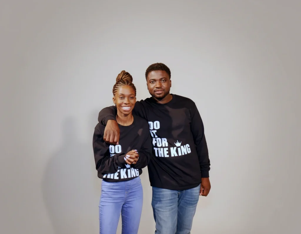 Couple wearing black Do It For The King Classic Long Sleeve shirts with bold white front print in a studio setting.
