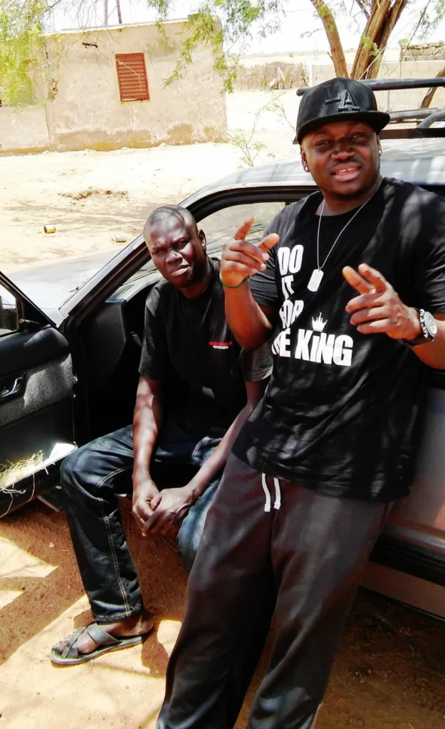 Two customers standing by a car outdoors, one wearing a black “Do It For The King” t-shirt, styled casually in a real-life setting.