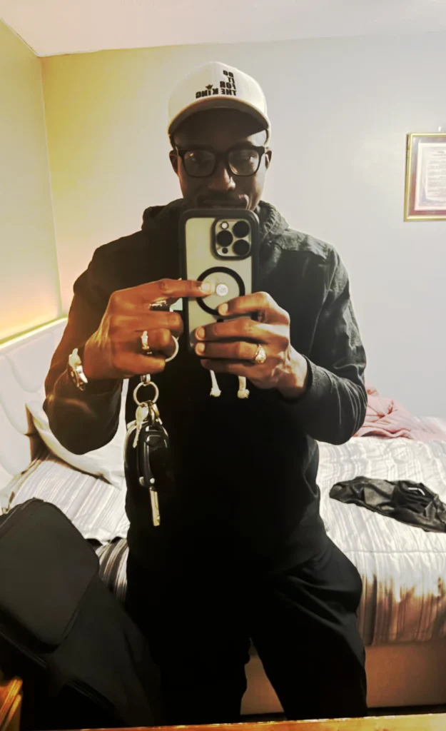 Customer taking a mirror photo while wearing a white “Do It For The King” fitted hat, styled with a clean casual outfit.